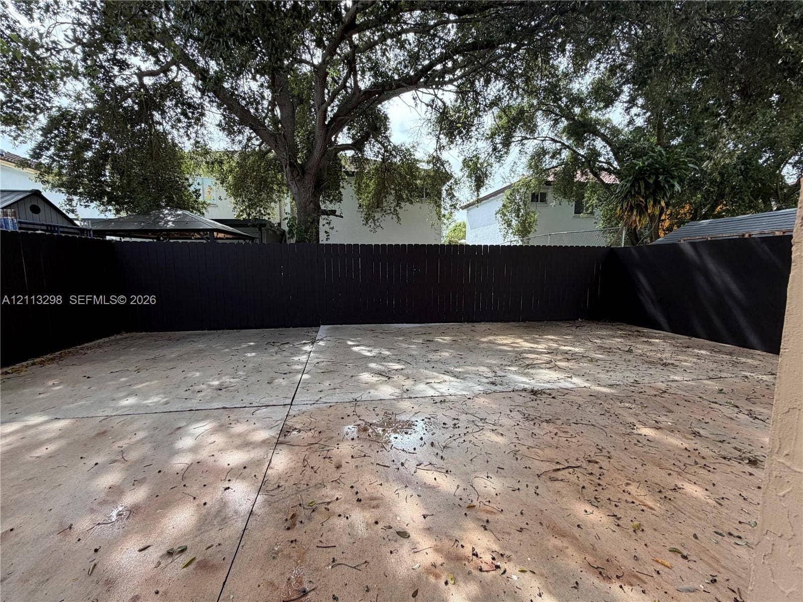 Concrete patio area enclosed by a dark wood-finish privacy fence with mature tree canopy overhead