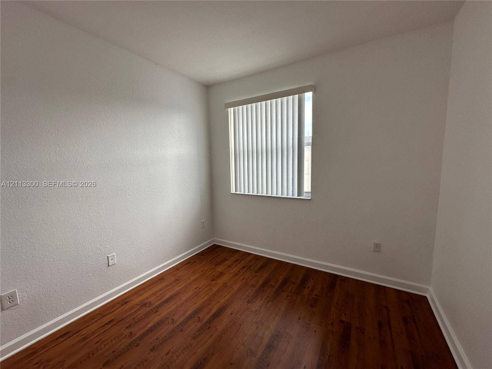 Interior room featuring wood-finish flooring, white walls, and a window with vertical blinds