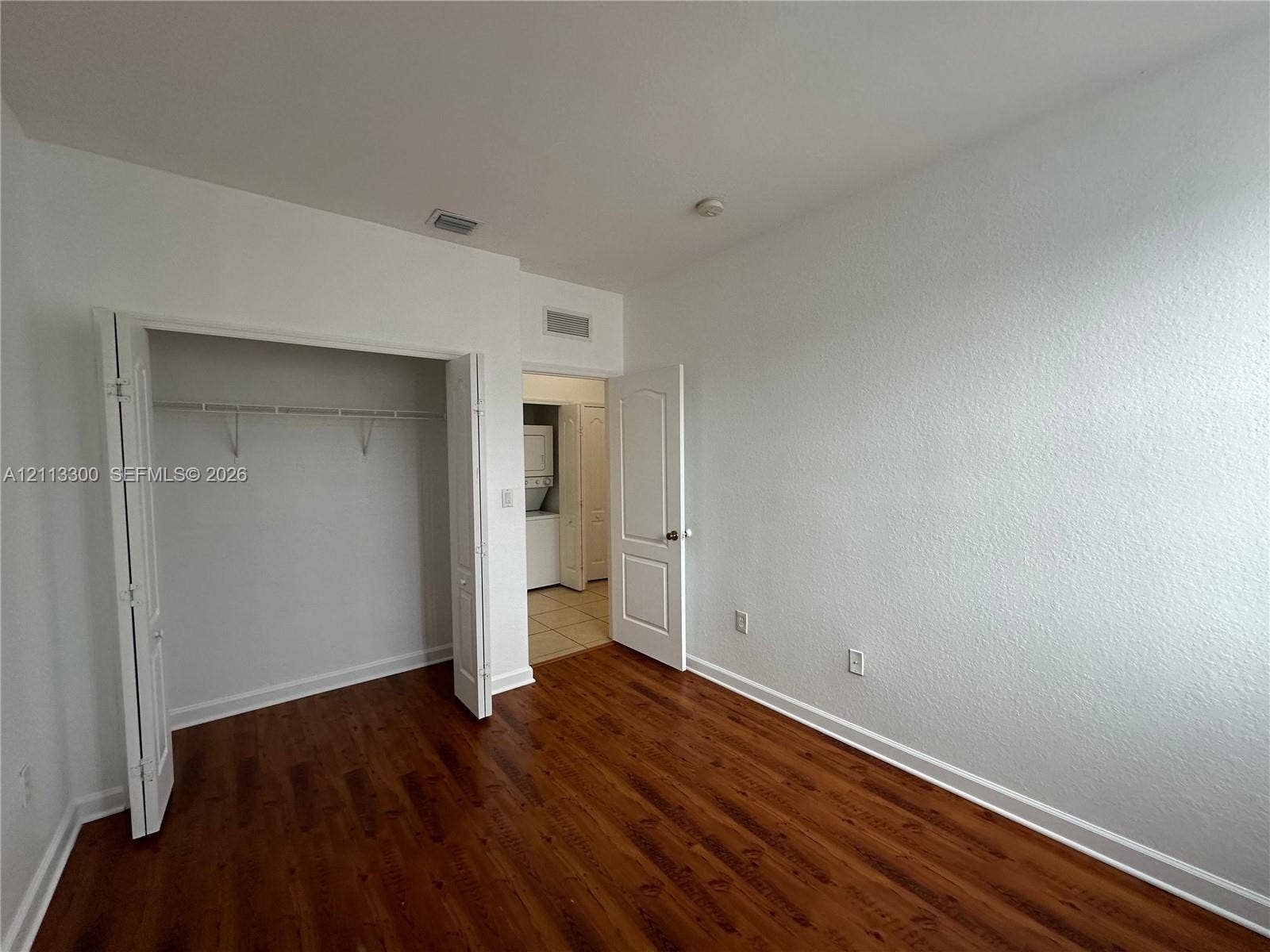 Room featuring wood-finish flooring, textured walls, and a closet with bifold doors