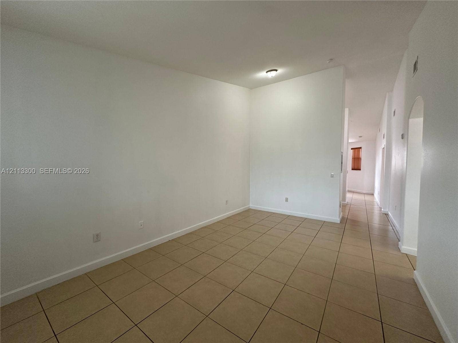 Neutral interior space featuring high ceilings, neutral wall tones, ceramic tile flooring, and an arched doorway