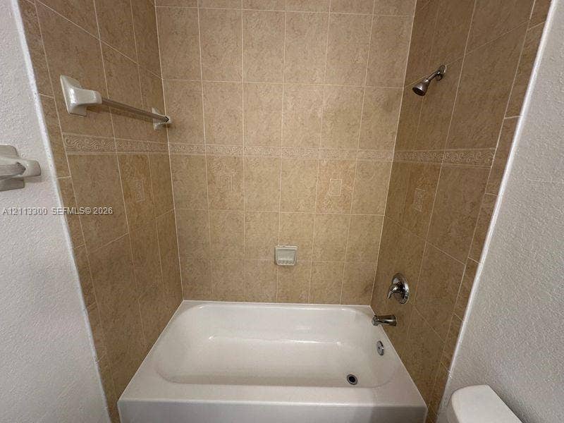 Bathtub surround featuring floor-to-ceiling neutral ceramic tiling, decorative accent border, built-in soap dish, and metal fixtures
