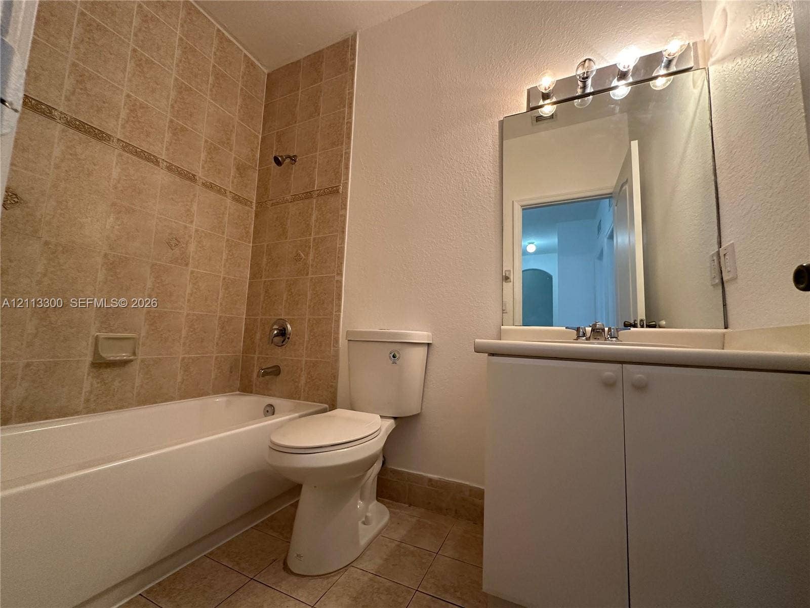 Bathroom featuring a tiled tub-shower surround, white vanity cabinet with a neutral countertop, built-in mirror with integrated lighting, and tile flooring