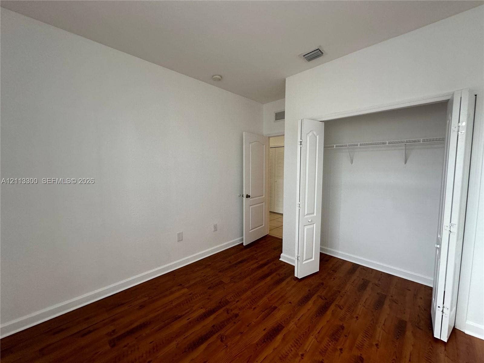 Room featuring wood-finish flooring, white walls, and a closet with bifold doors and built-in shelving