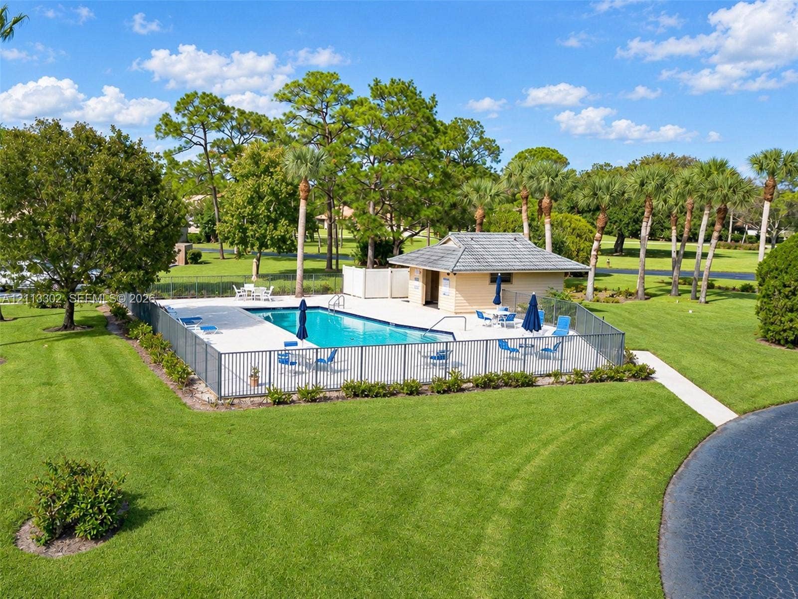 9450 Meadowood Drive, #202, Fort Pierce, FL 34951 In-ground swimming pool featuring a concrete deck, metal perimeter fencing, and a detached pool house with a shingle roof