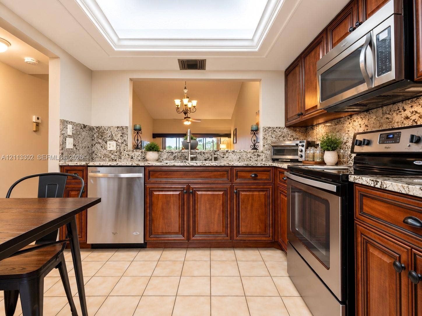 9450 Meadowood Drive, #202, Fort Pierce, FL 34951 Kitchen featuring custom stained wood cabinetry, stone countertops, stainless steel appliances, tiled flooring, and a recessed ceiling skylight