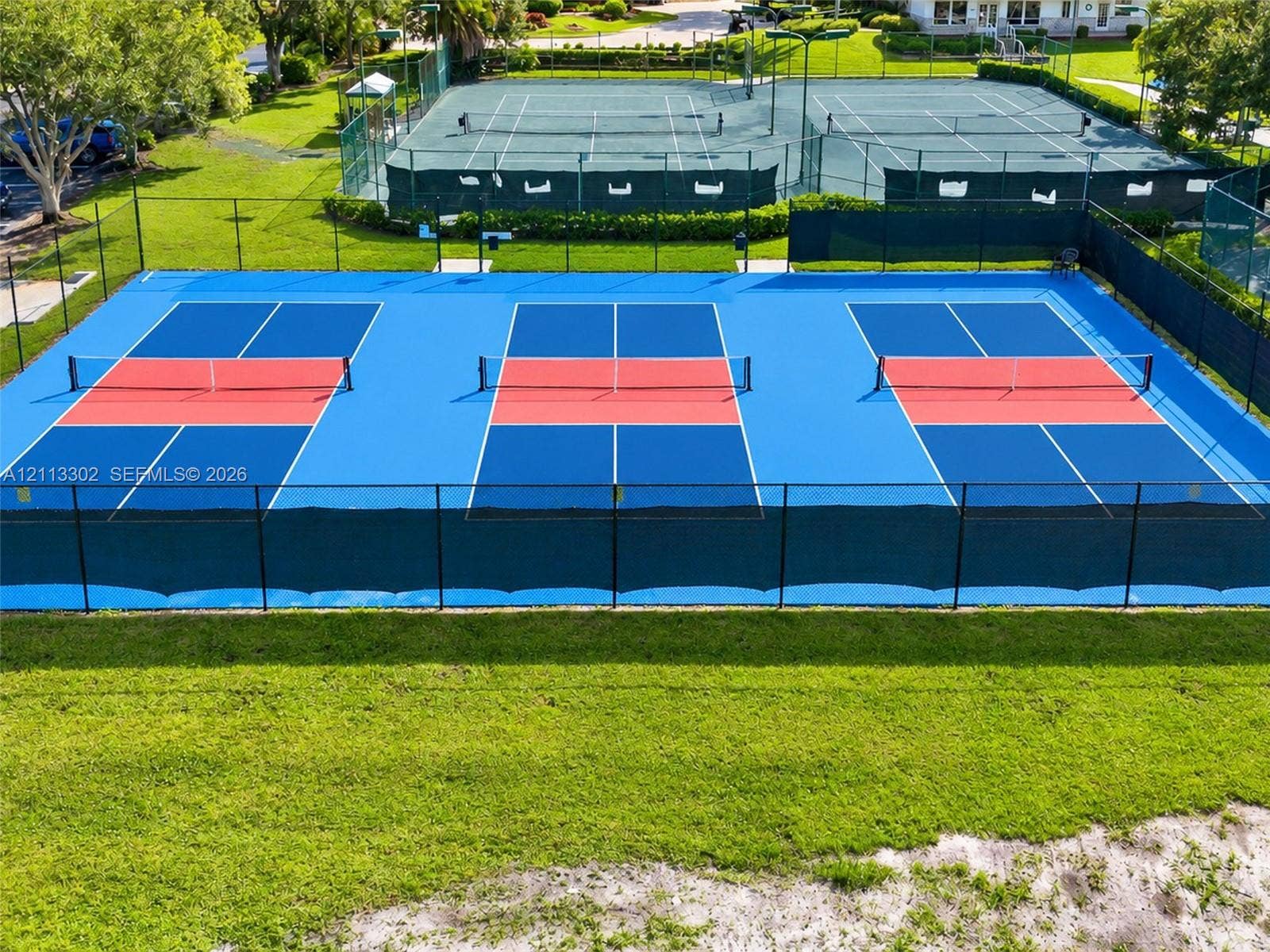 9450 Meadowood Drive, #202, Fort Pierce, FL 34951 Triple pickleball court featuring a multi-toned blue and red synthetic surface, perimeter chain-link fencing, and integrated nets