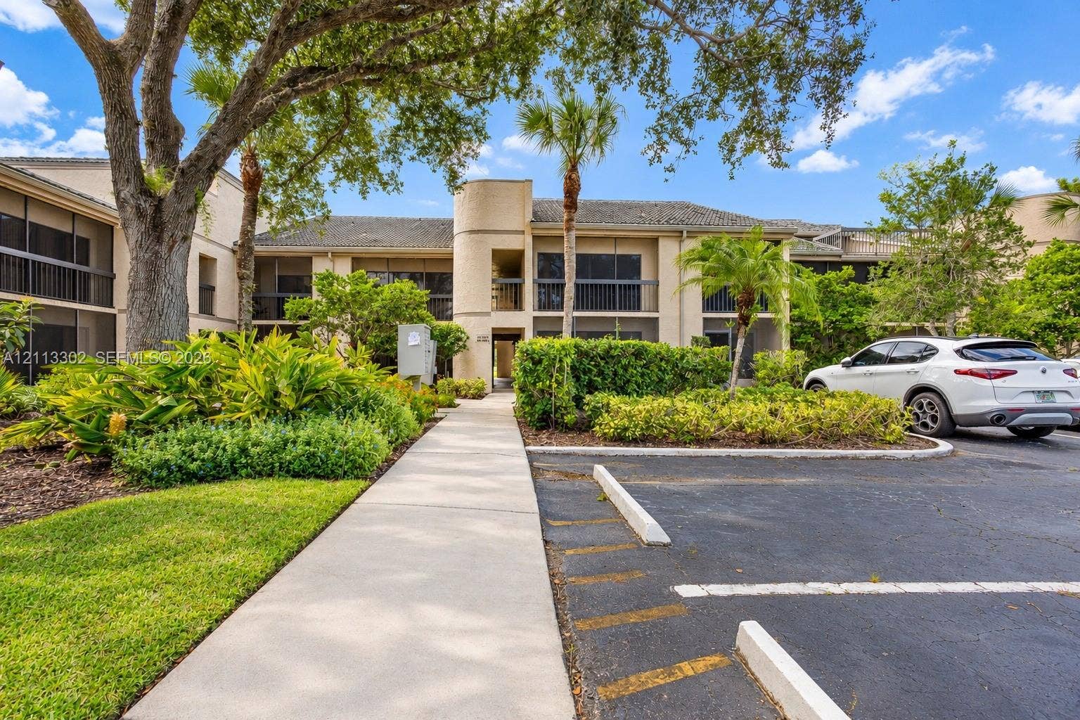 9450 Meadowood Drive, #202, Fort Pierce, FL 34951 Multi-story exterior featuring a neutral stucco facade, screened balconies, mature shade trees, and manicured landscaping