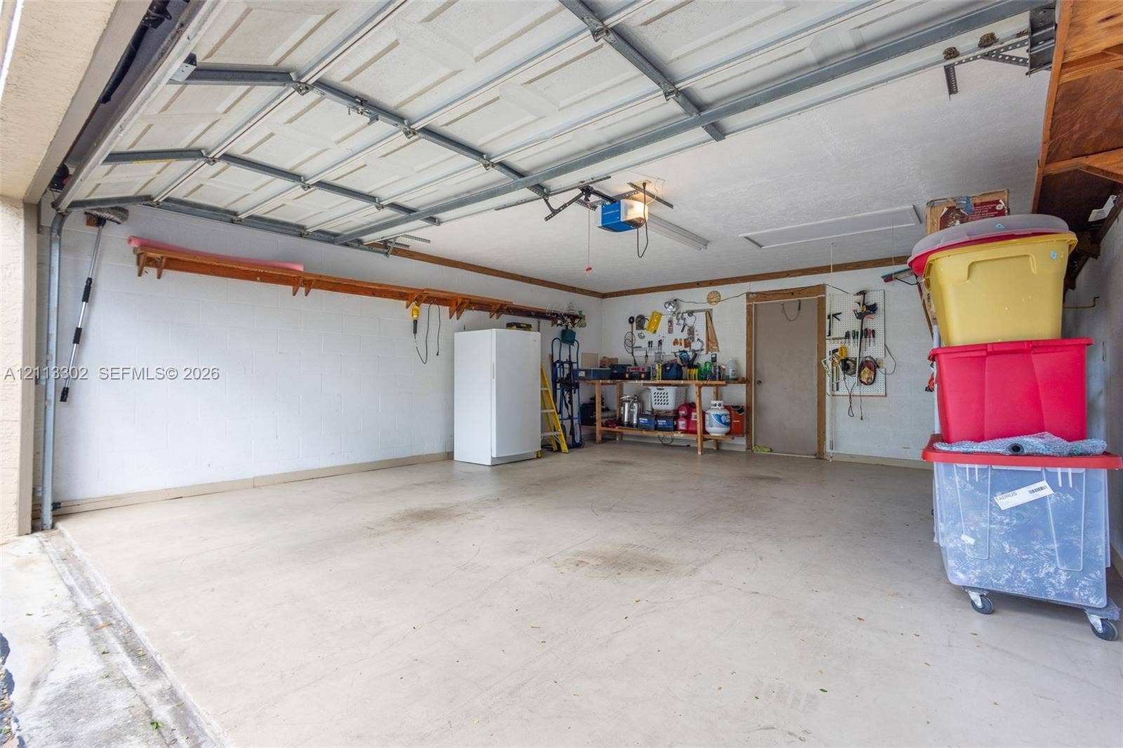 9450 Meadowood Drive, #202, Fort Pierce, FL 34951 Multi-car garage featuring a concrete floor, overhead automatic door, and wall-mounted storage shelving