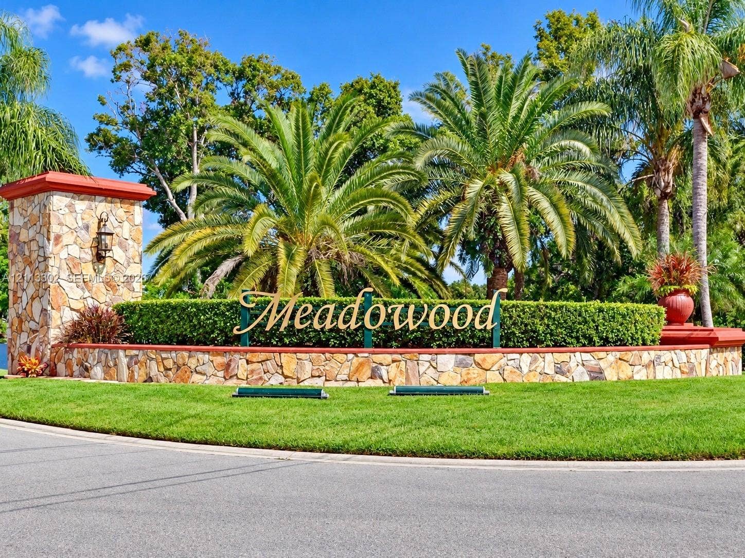 9450 Meadowood Drive, #202, Fort Pierce, FL 34951 Stone masonry monument entrance featuring manicured hedging, mature palm trees, and structural accent lighting