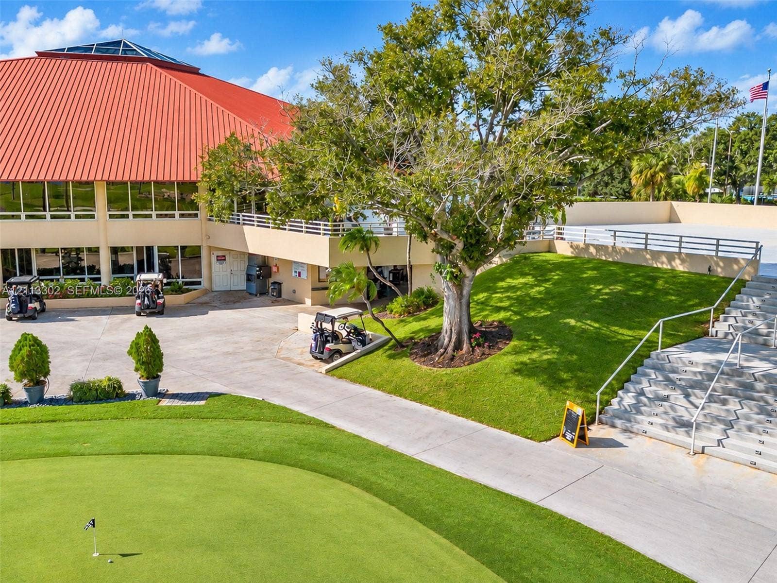 9450 Meadowood Drive, #202, Fort Pierce, FL 34951 Red metal roof structure with large skylight, multi-level concrete stairs with metal railings, manicured green space, and golf course access