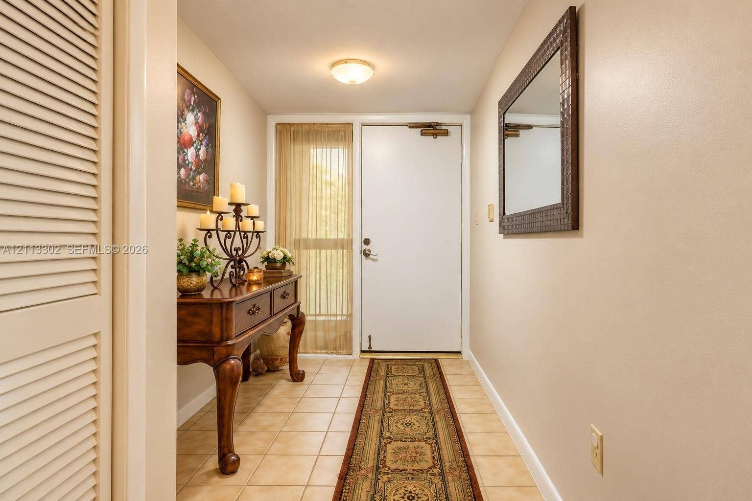 9450 Meadowood Drive, #202, Fort Pierce, FL 34951 Entryway featuring neutral-toned tile flooring, louvered closet doors, and a glass-paneled sidelight with vertical blinds
