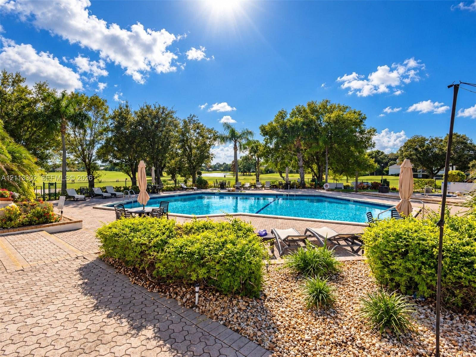 9450 Meadowood Drive, #202, Fort Pierce, FL 34951 Outdoor swimming pool surrounded by a brick paver deck, manicured hedges, and mature trees
