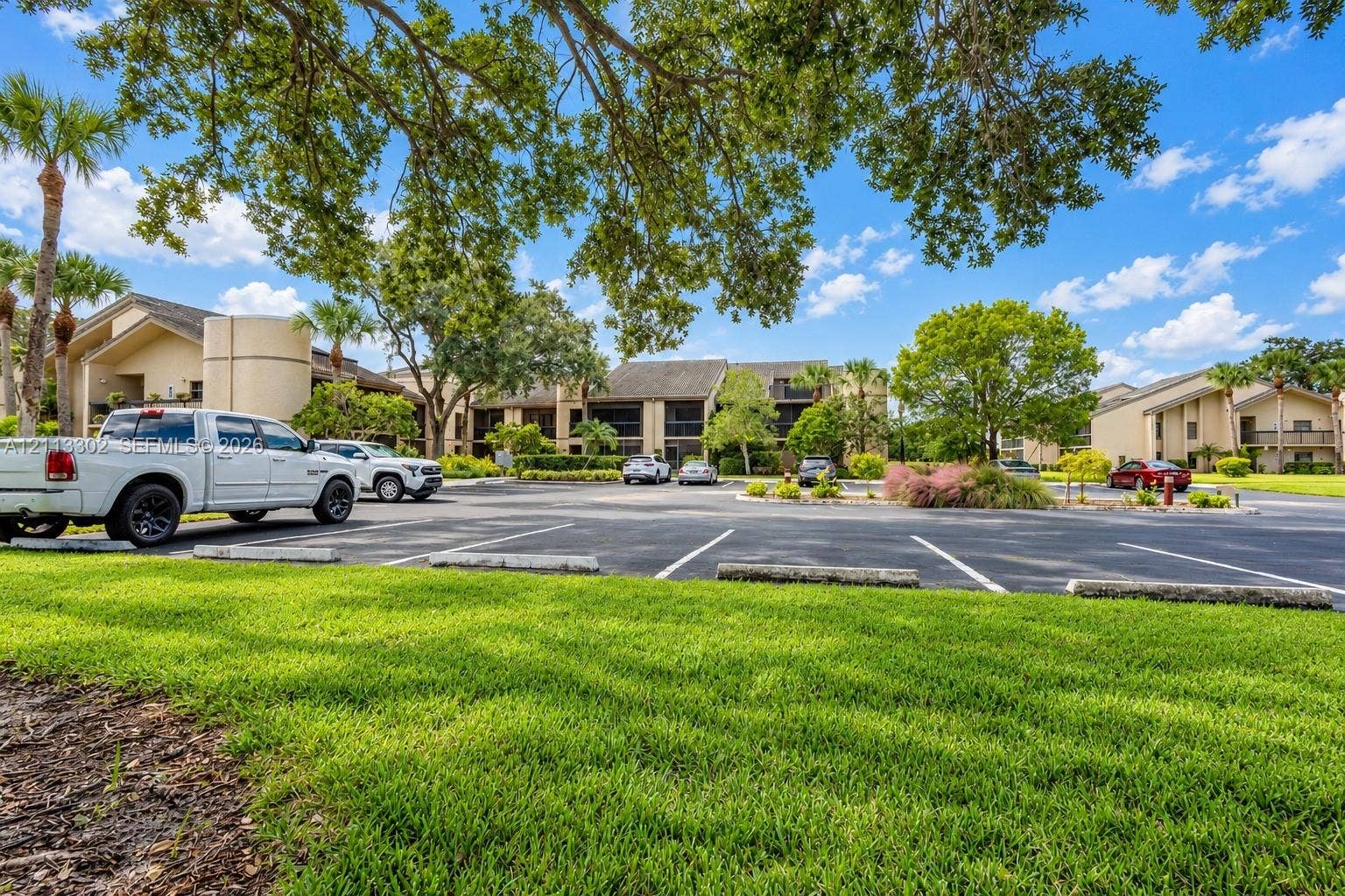 9450 Meadowood Drive, #202, Fort Pierce, FL 34951 Exterior grounds featuring paved parking, expansive green space, mature canopy trees, and landscaped shrubbery surrounding multi-story buildings