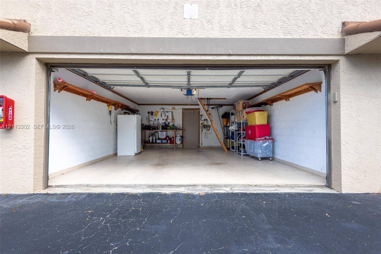 9450 Meadowood Drive, #202, Fort Pierce, FL 34951 Attached two-car garage featuring painted masonry walls, overhead sectional door, built-in wooden wall shelving, and an integrated workbench