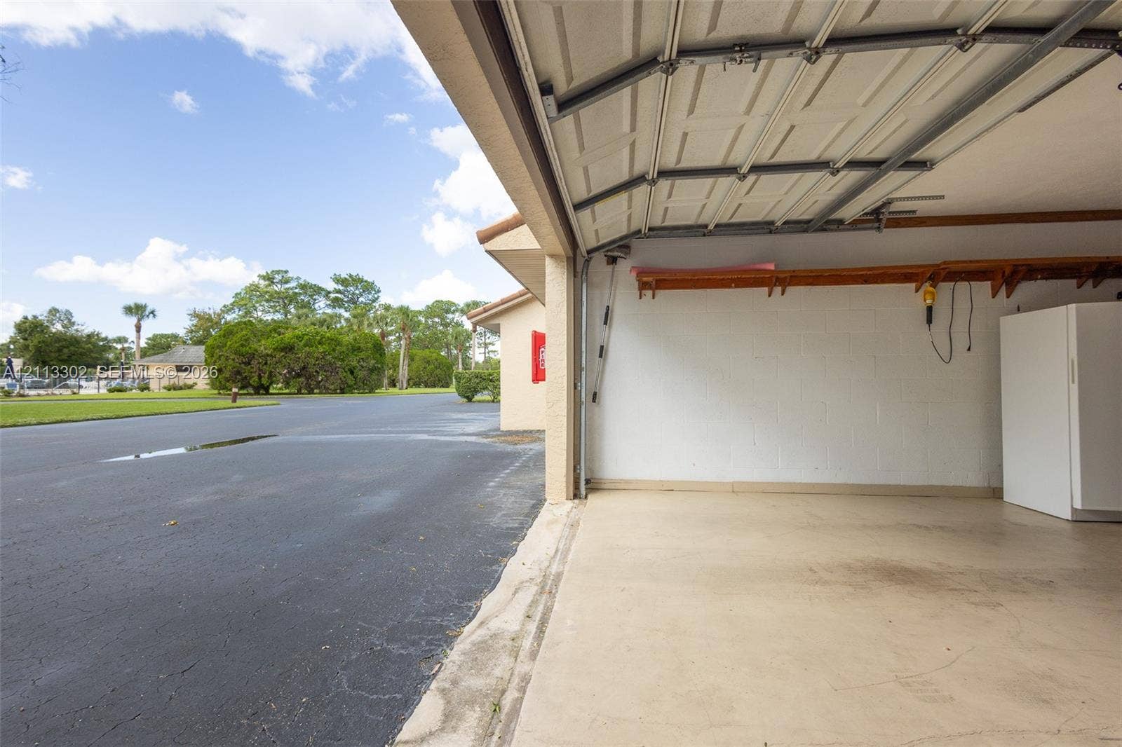 9450 Meadowood Drive, #202, Fort Pierce, FL 34951 Garage interior featuring painted concrete block walls, a concrete floor, overhead door tracks, and built-in wood shelving