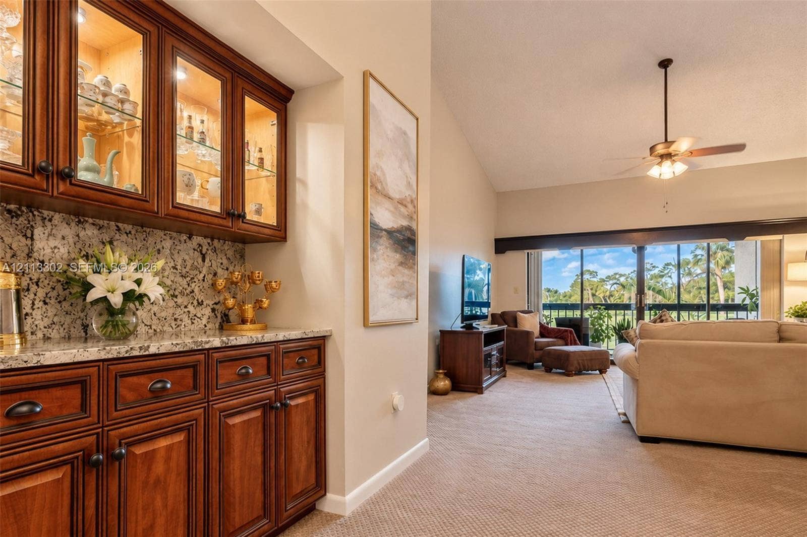 9450 Meadowood Drive, #202, Fort Pierce, FL 34951 Built-in wood cabinetry with glass-front upper displays, stone countertops, vaulted ceilings, and a ceiling fan