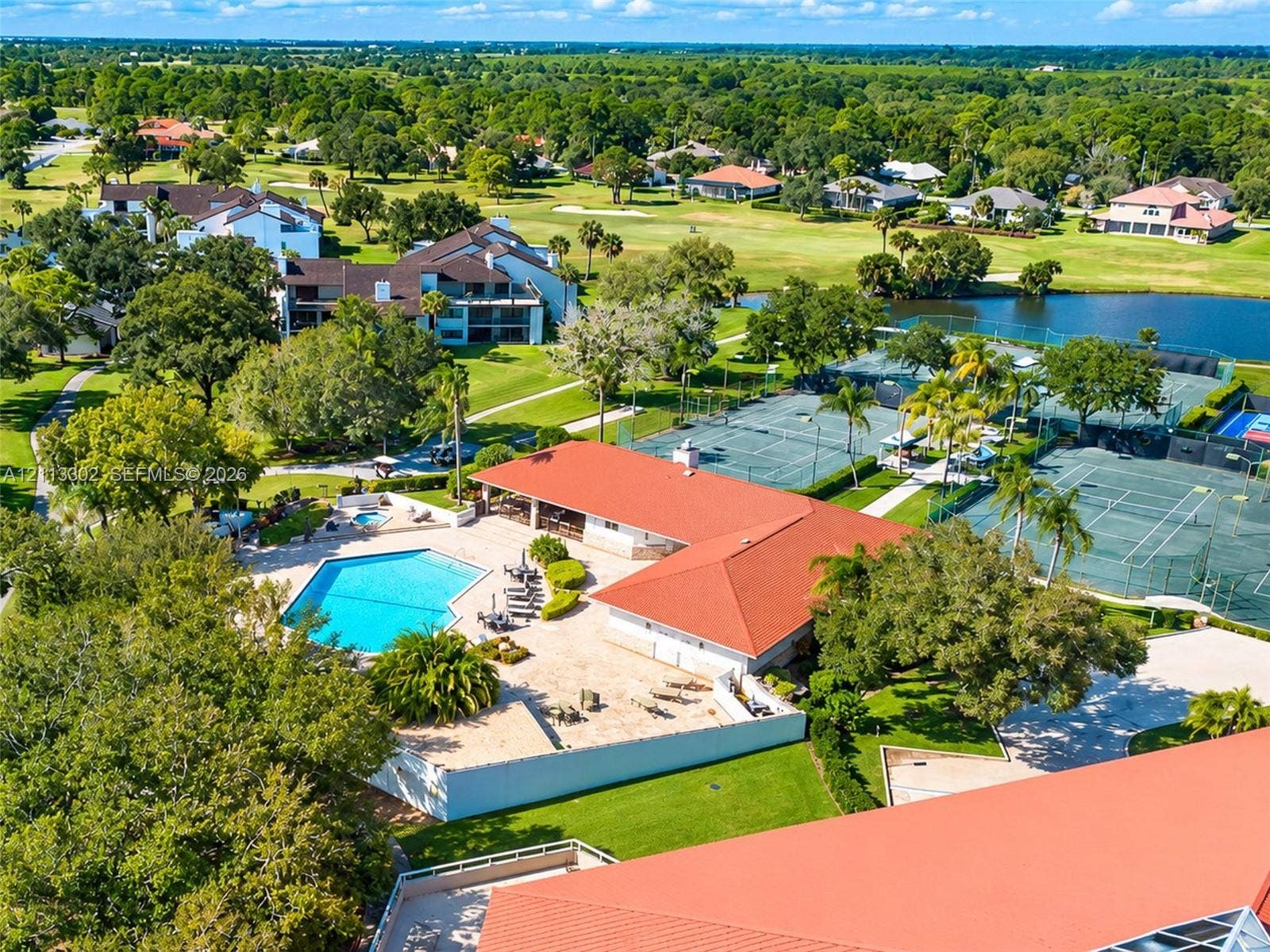9450 Meadowood Drive, #202, Fort Pierce, FL 34951 Community recreation center featuring an outdoor swimming pool, multiple tennis courts, a red tile roof, and expansive surrounding lawn areas