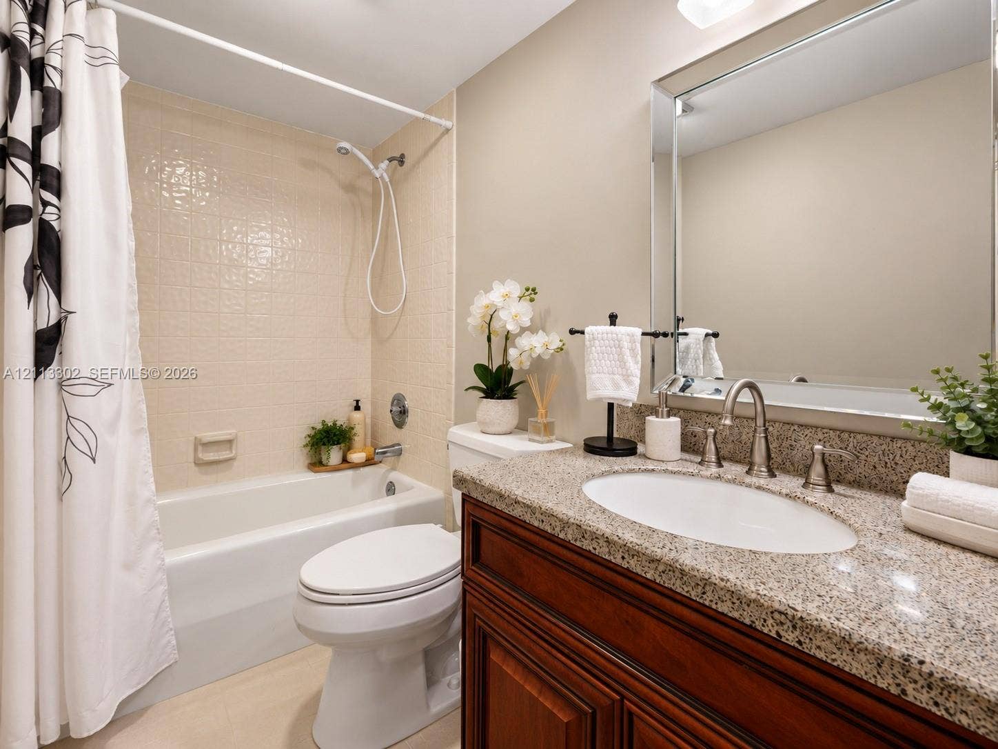 9450 Meadowood Drive, #202, Fort Pierce, FL 34951 Bathroom featuring a stone-composite countertop, dark wood-finish cabinetry, undermount oval sink, framed wall mirror, and a tiled shower-tub combination with a handheld showerhead