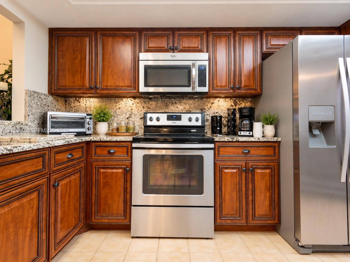 9450 Meadowood Drive, #202, Fort Pierce, FL 34951 Kitchen featuring stained wood cabinetry, natural stone countertops, tile flooring, and stainless steel appliances including a built-in microwave and range