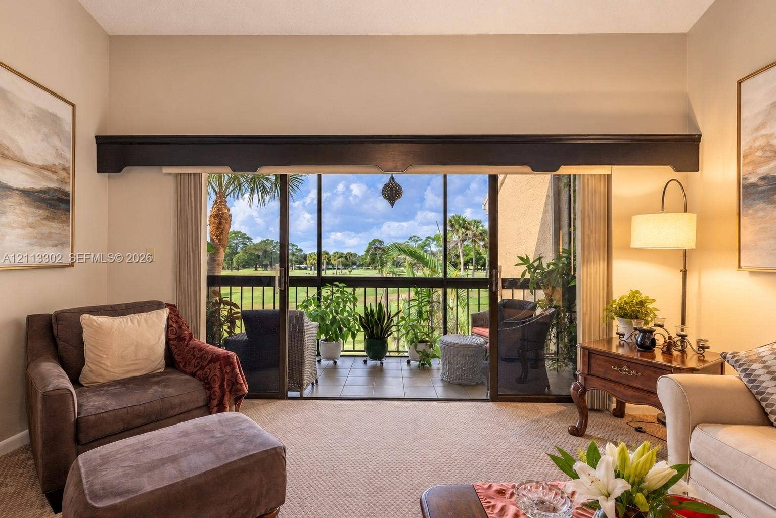 9450 Meadowood Drive, #202, Fort Pierce, FL 34951 Living space featuring high ceilings, decorative valance, and sliding glass doors leading to a screened balcony with tiled flooring and metal railing