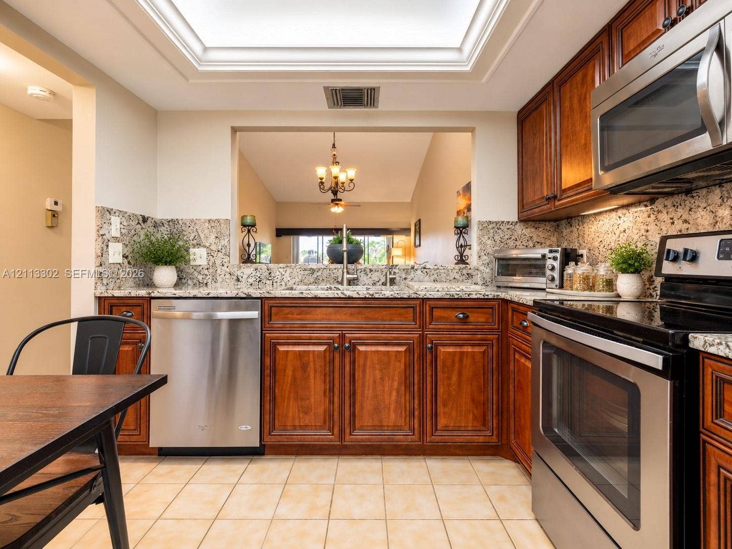 9450 Meadowood Drive, #202, Fort Pierce, FL 34951 Kitchen featuring wood cabinetry, stone countertops, stainless steel appliances, a recessed skylight, and tile flooring
