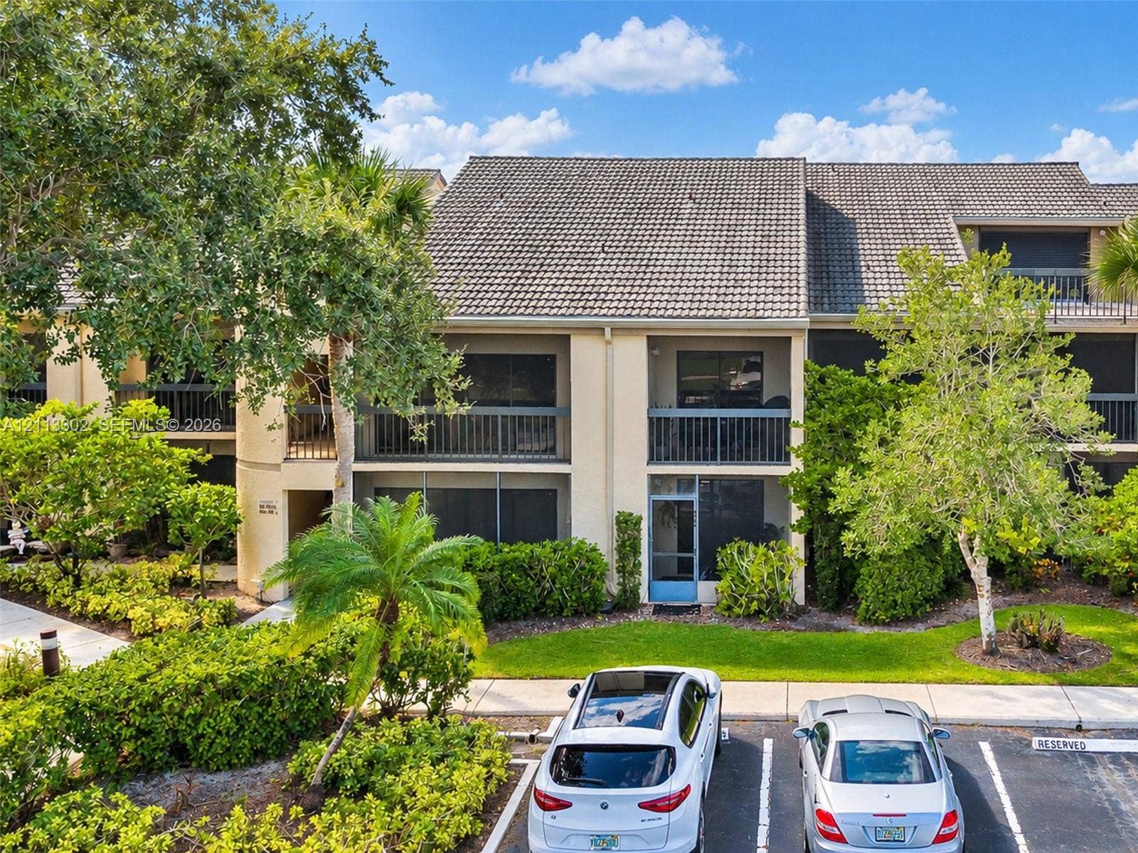 9450 Meadowood Drive, #202, Fort Pierce, FL 34951 Multi-story building exterior featuring a tile roof, private screened-in balconies, and structured hardscaping surrounded by mature landscaping