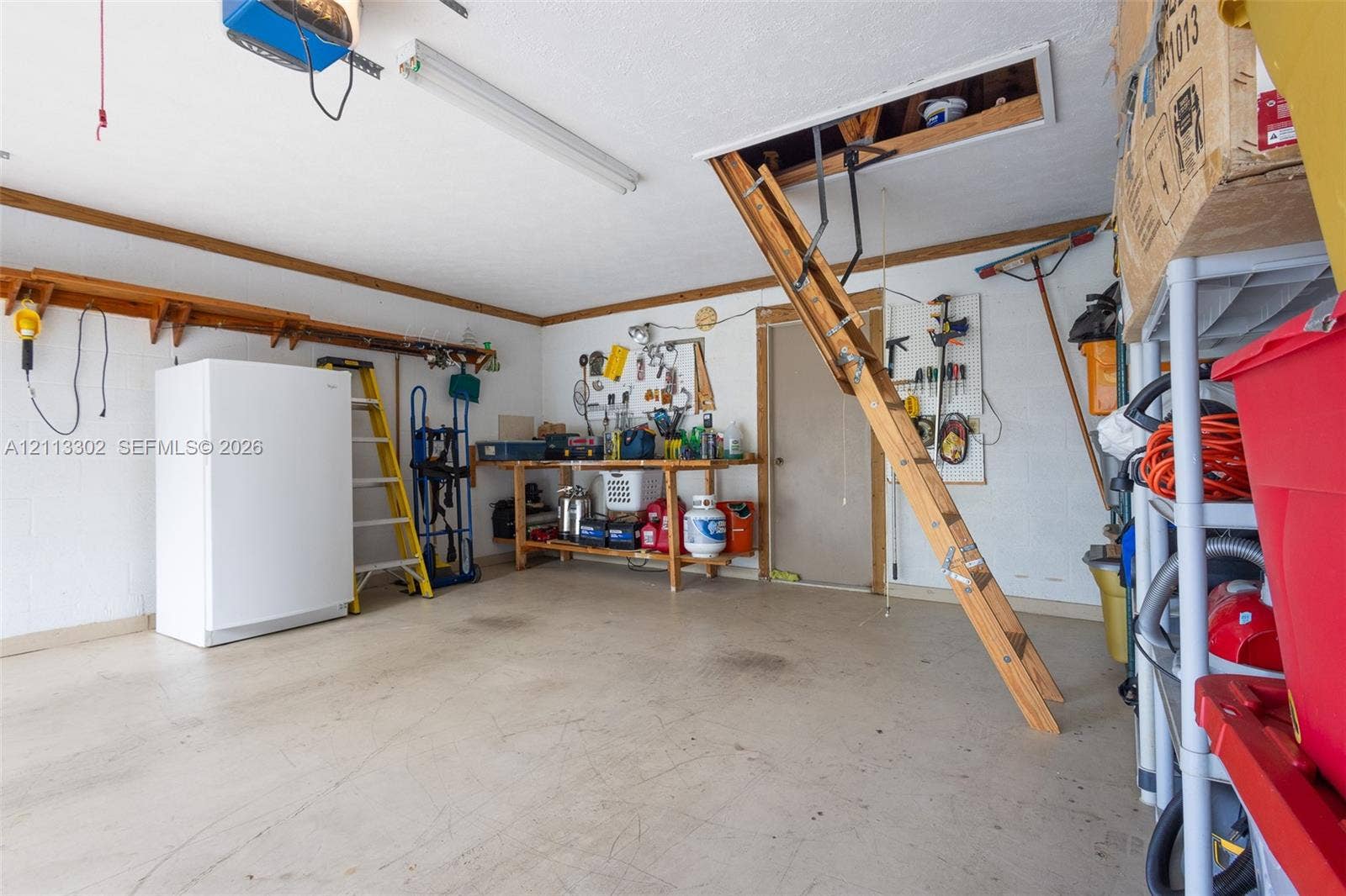 9450 Meadowood Drive, #202, Fort Pierce, FL 34951 Garage space featuring a pull-down wooden attic ladder, a built-in workbench, overhead fluorescent lighting, and wall-mounted shelving