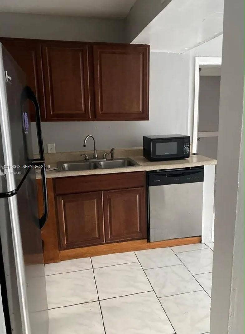 Lauderdale Lakes, FL 33313 Kitchen featuring wood-finish cabinetry, stainless steel appliances, a double-basin sink, and tile flooring