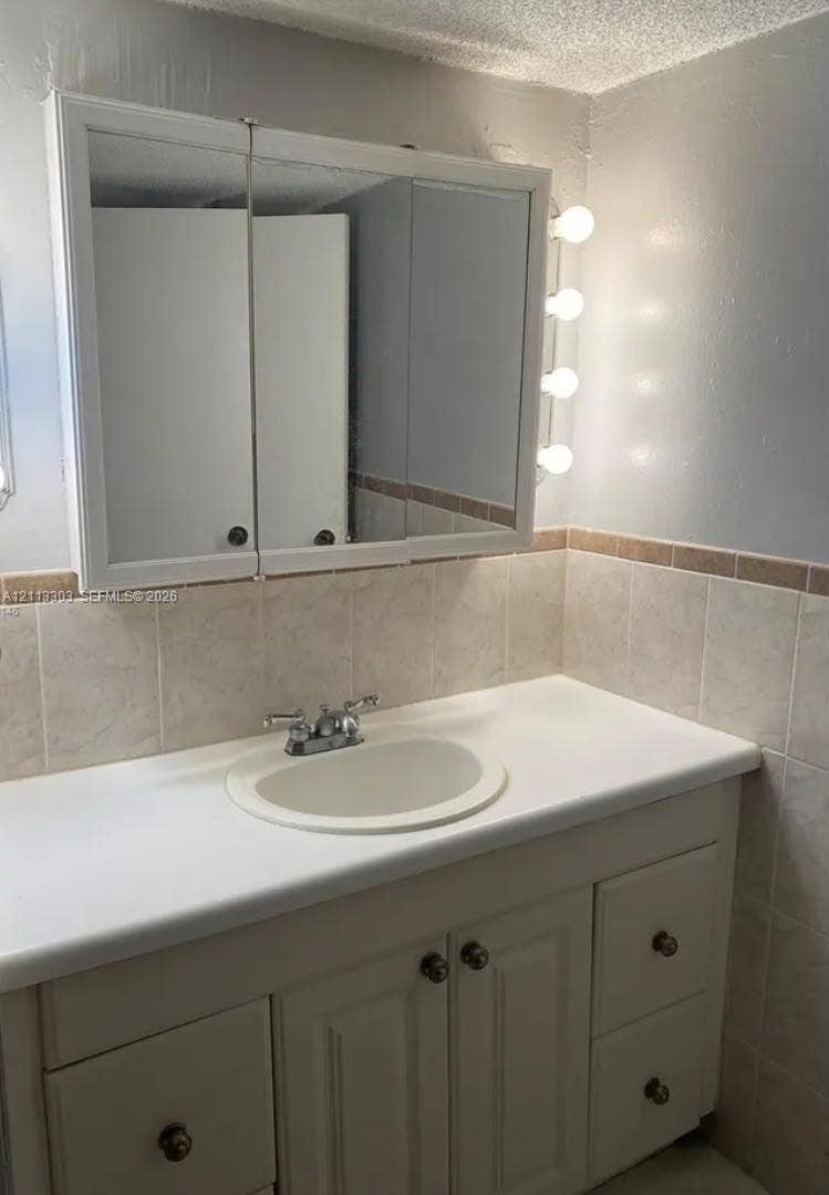 Lauderdale Lakes, FL 33313 Vanity featuring built-in cabinetry with drawers, solid surface countertop, integrated basin, tri-fold mirrored medicine cabinet, and vertical lighting fixtures, accented by tile wainscoting