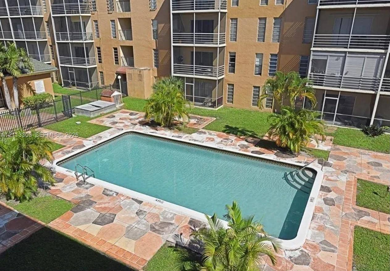 Lauderdale Lakes, FL 33313 Rectangular swimming pool with metal ladder and steps, surrounded by multi-colored stone paver decking, manicured lawn, and mature palm trees