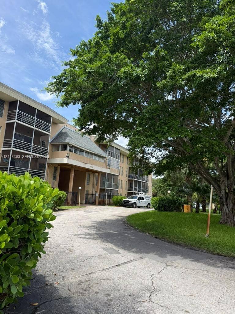 Lauderdale Lakes, FL 33313 Multi-story exterior featuring screened balconies, shingle roofing, asphalt paving, and mature landscaping