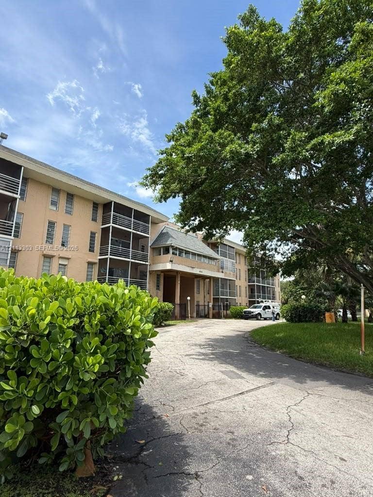 Lauderdale Lakes, FL 33313 Multi-story building exterior featuring screened balconies, stucco facade, mature trees, and landscaped grounds