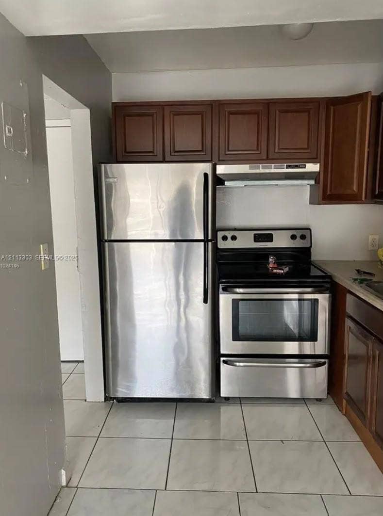 Lauderdale Lakes, FL 33313 Kitchen featuring wood cabinetry, stainless steel refrigerator, stainless steel electric range, range hood, and tile flooring