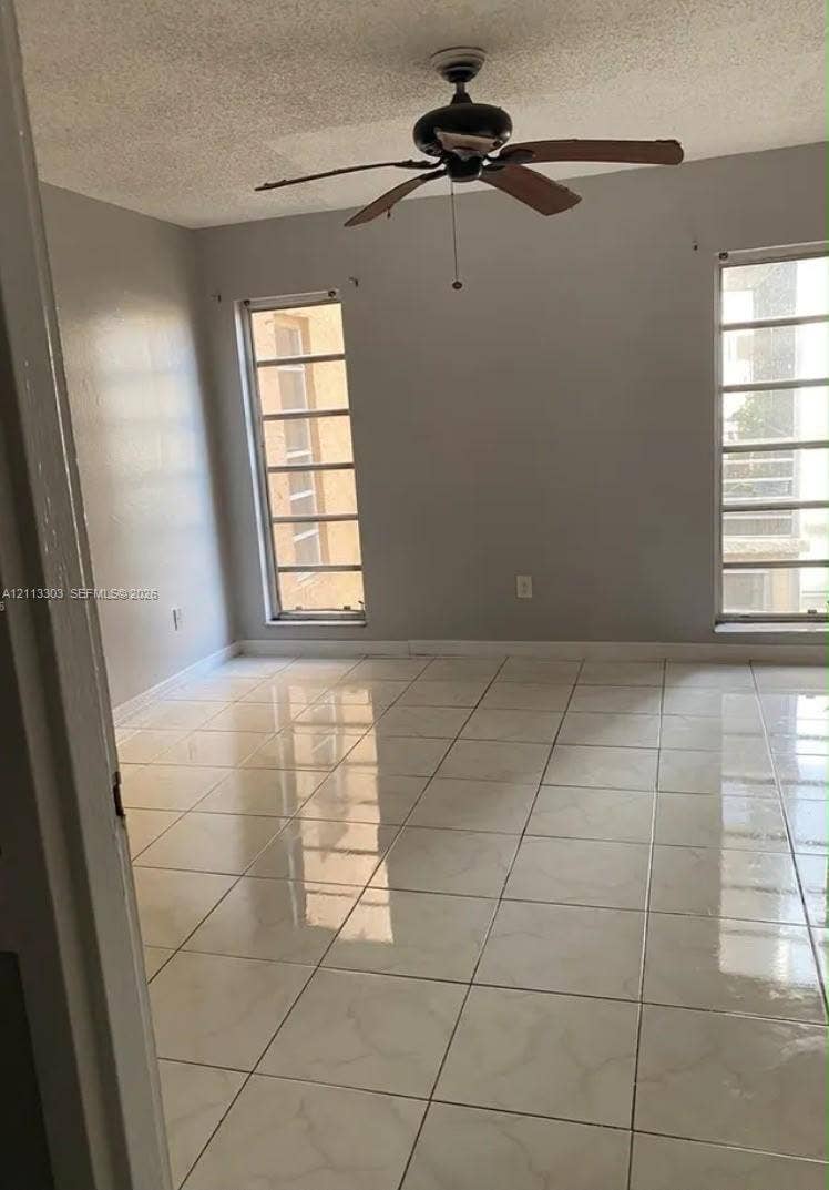 Lauderdale Lakes, FL 33313 Room interior featuring large-format tile flooring, dual floor-to-ceiling windows with grid muntins, and a central ceiling fan
