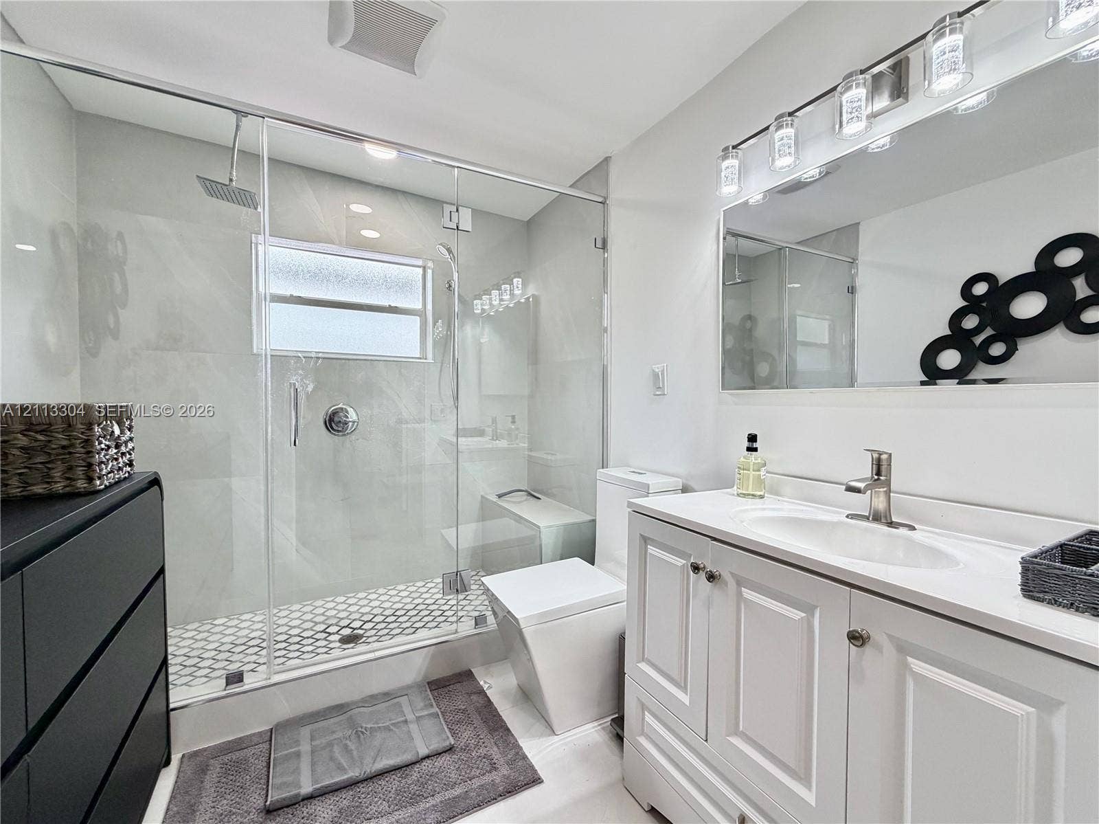 1810 SW 5th Avenue, #n/a, Miami, Miami, FL 33129 Bathroom featuring a frameless glass-enclosed shower with large-format wall tile and hexagonal floor tile, a white vanity cabinet with an integrated sink, and a multi-bulb light fixture above a wide mirror