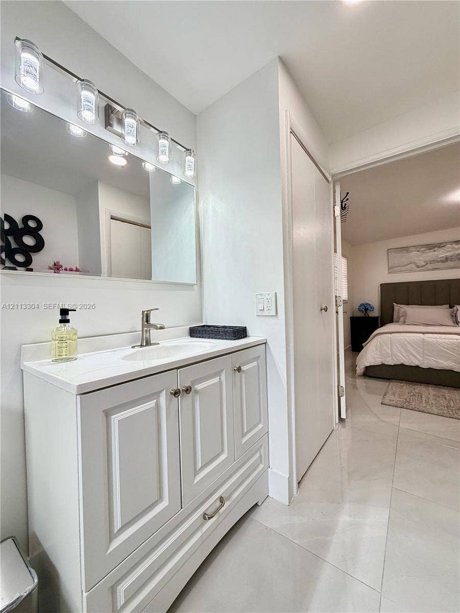 1810 SW 5th Avenue, #n/a, Miami, Miami, FL 33129 White vanity with shaker-style cabinetry, solid-surface countertop with an integrated sink, polished metal hardware, and a multi-bulb light fixture mounted above a rectangular mirror