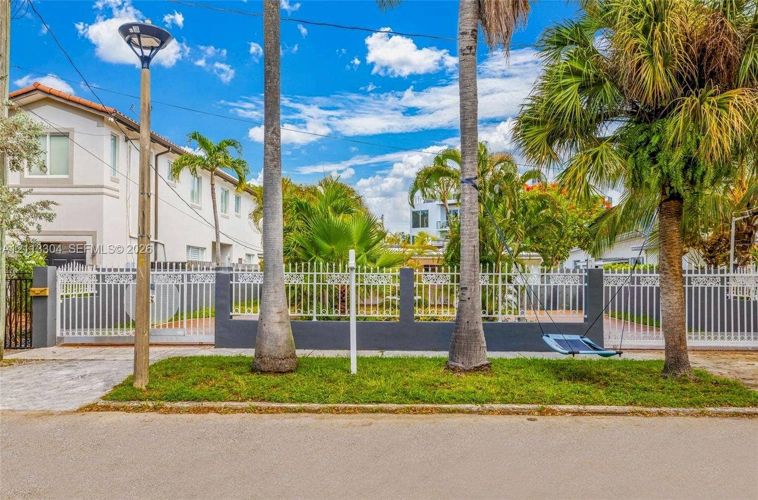 1810 SW 5th Avenue, #n/a, Miami, Miami, FL 33129 Exterior street-level view featuring a decorative metal perimeter fence with masonry pillars, manicured grass area, mature palm trees, and exterior post lighting