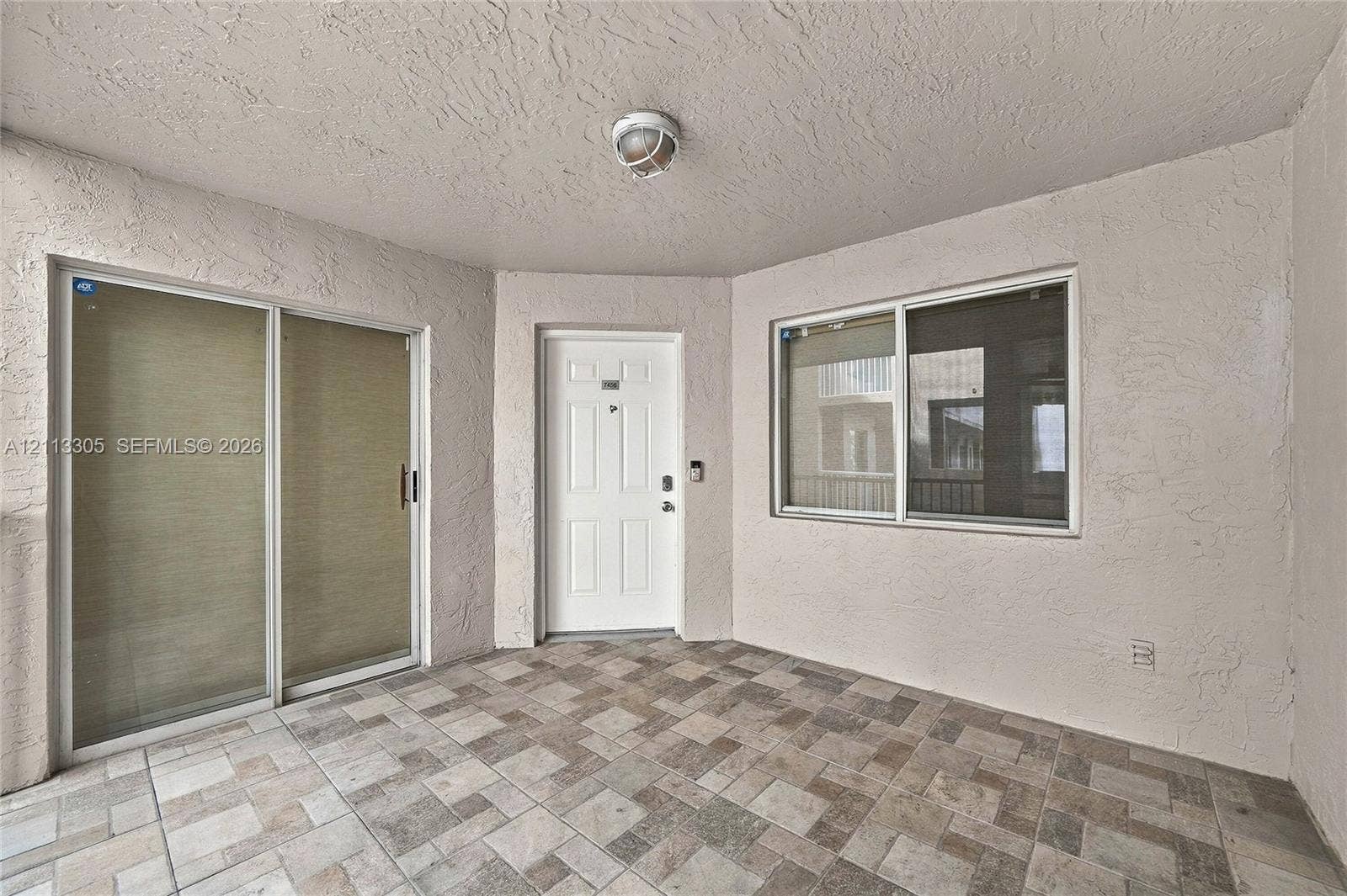 Covered entryway featuring textured wall finishes, multi-tonal ceramic tile flooring, a six-panel entry door, and a sliding glass door