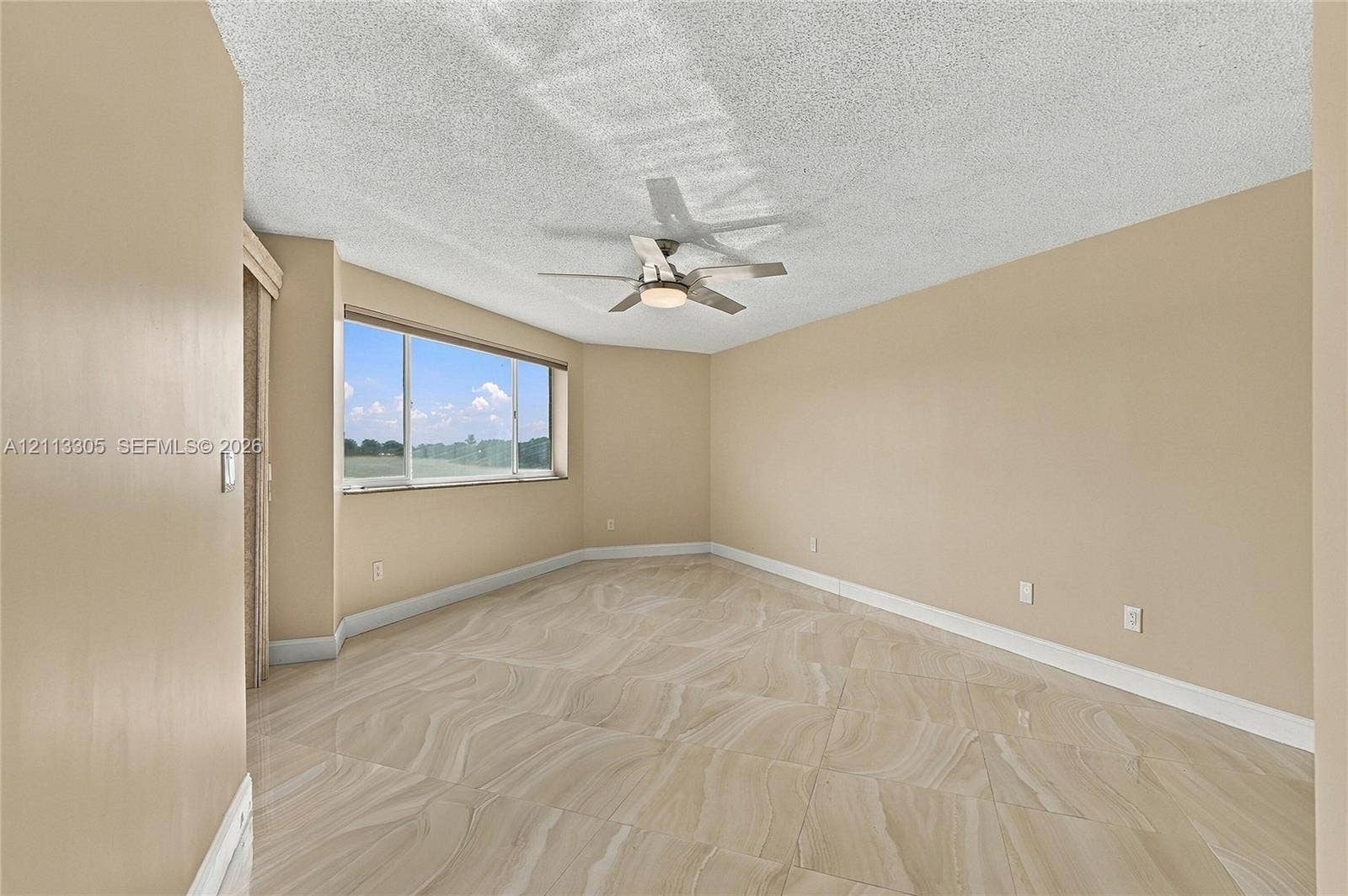 Room featuring large-format tile flooring, a textured ceiling, a ceiling fan with integrated lighting, and a wide window