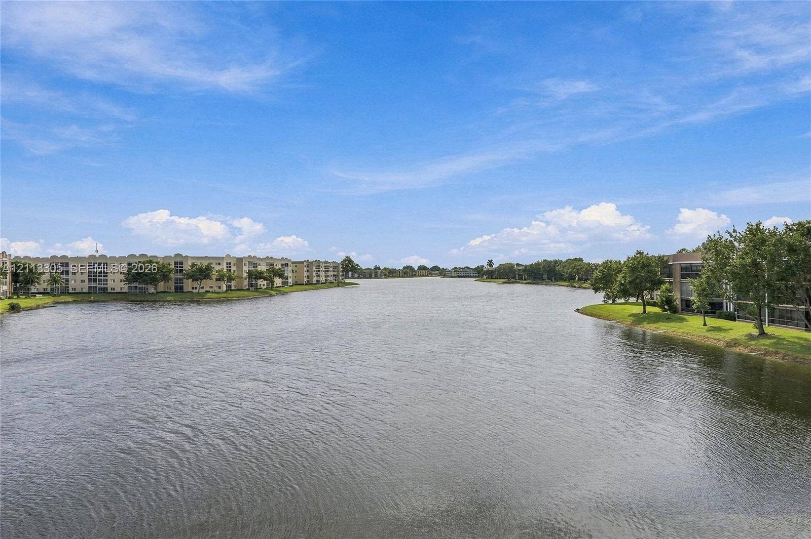 Expansive water frontage featuring a central lake, landscaped grass perimeters, and surrounding multi-level residential structures