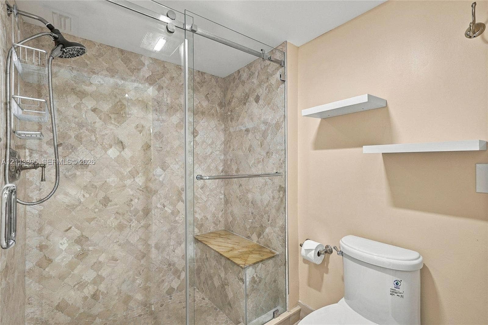 Walk-in shower featuring glass sliding doors, stone-tile surround, a built-in stone bench, a multi-setting showerhead, and two wall-mounted floating shelves