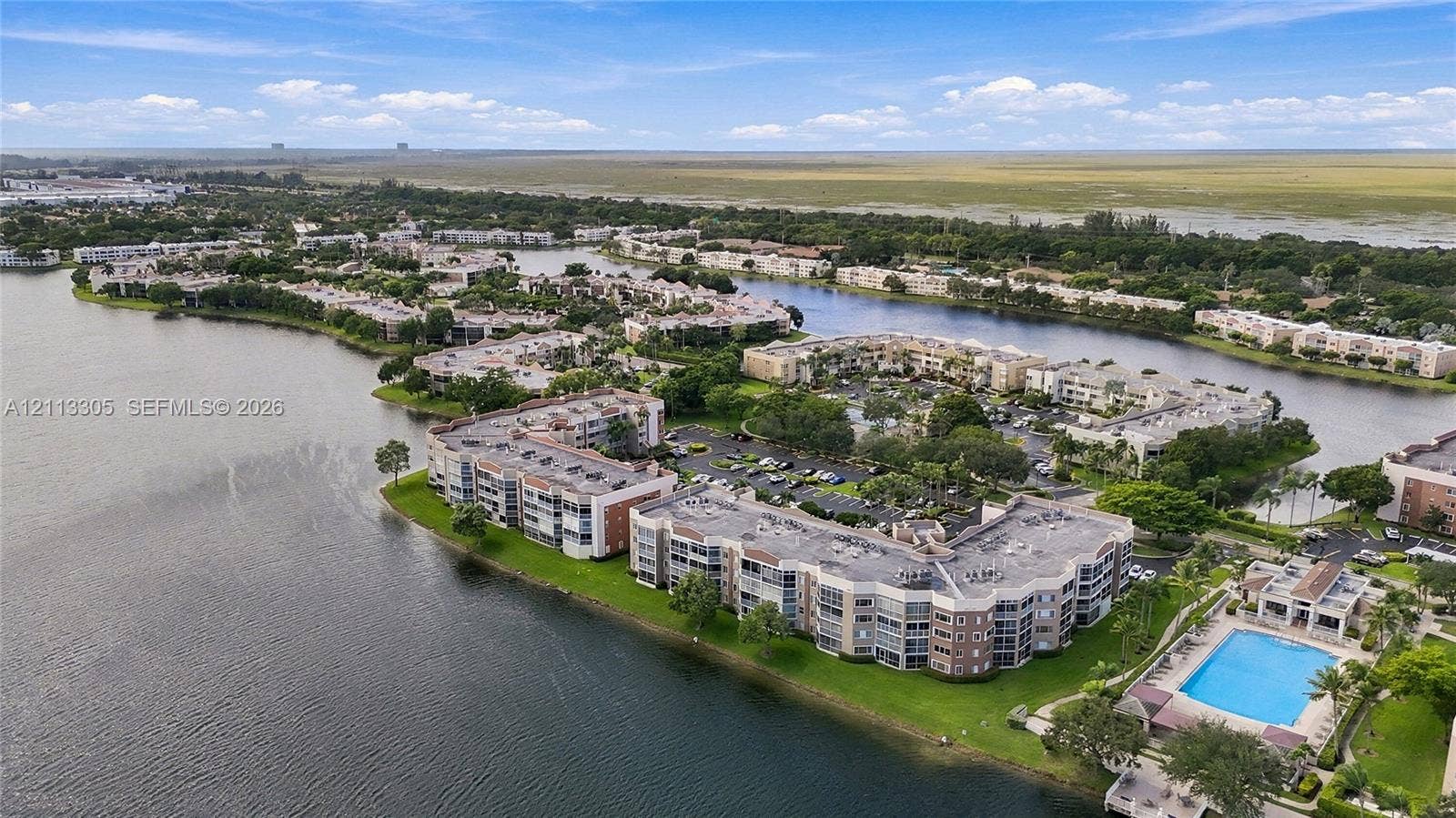 Aerial perspective of waterfront multi-family residential structures featuring expansive canal frontage, lush green landscaping, and a community swimming pool