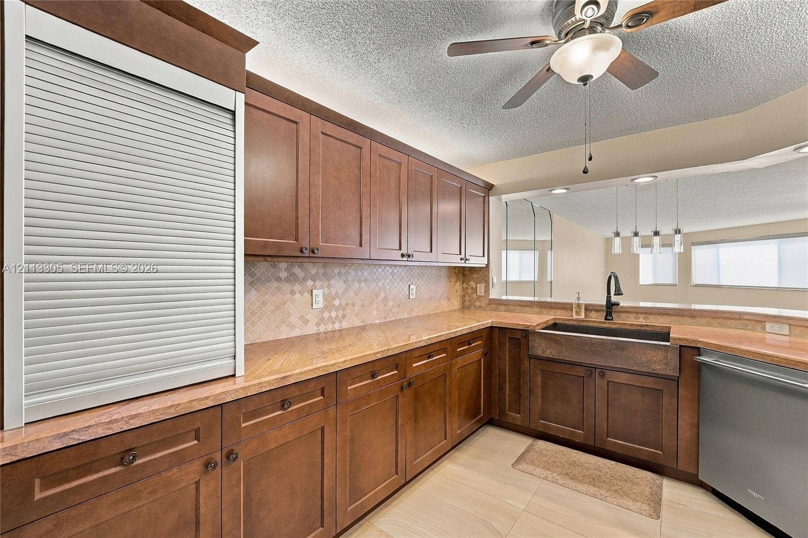 Kitchen featuring dark wood cabinetry, integrated roll-top appliance garage, tiled backsplash, farmhouse-style sink with matte black faucet, and stone countertops