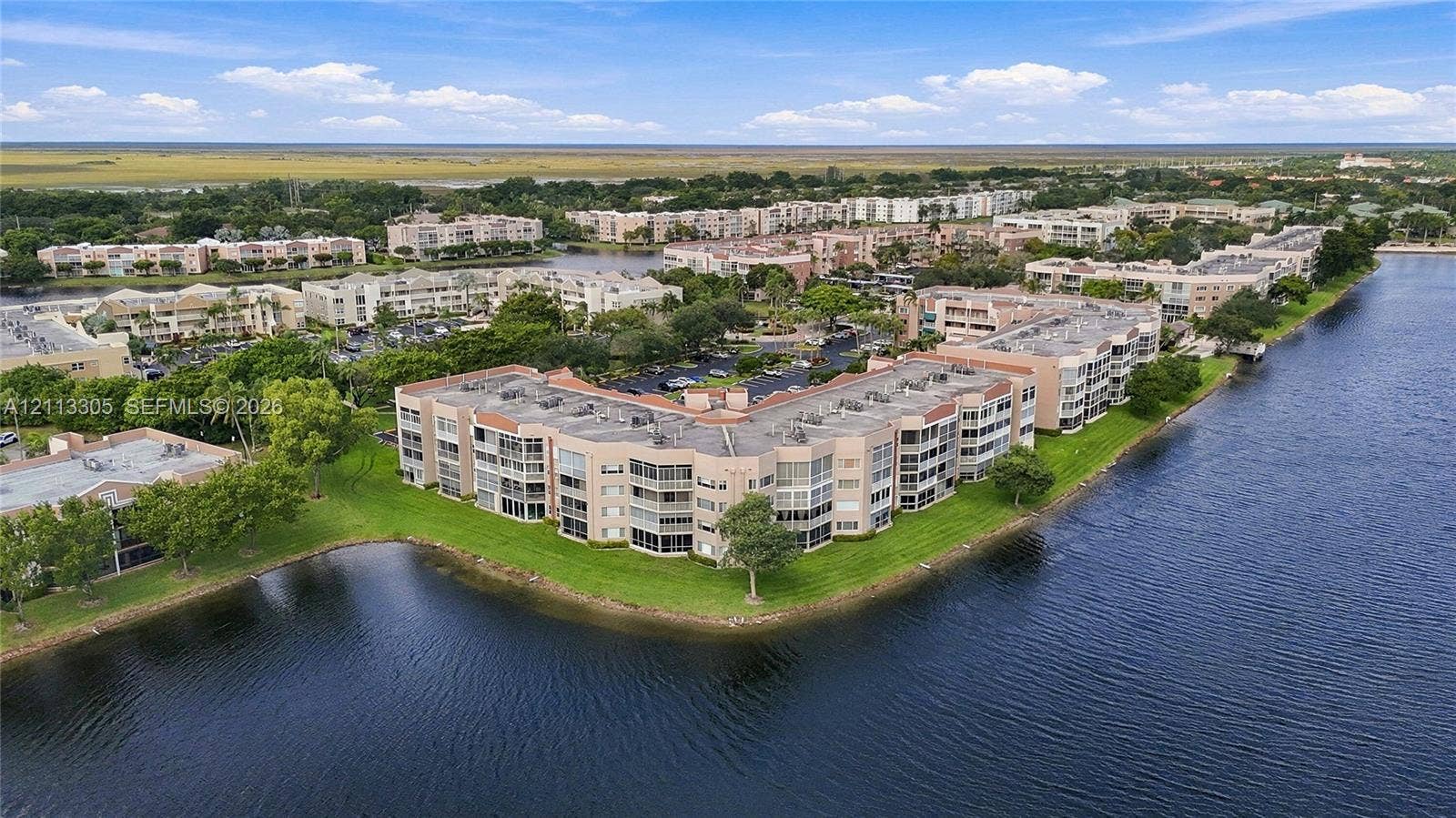 Aerial perspective of a multi-story residential complex situated on a waterfront lot featuring mature landscaping and a expansive lawn perimeter