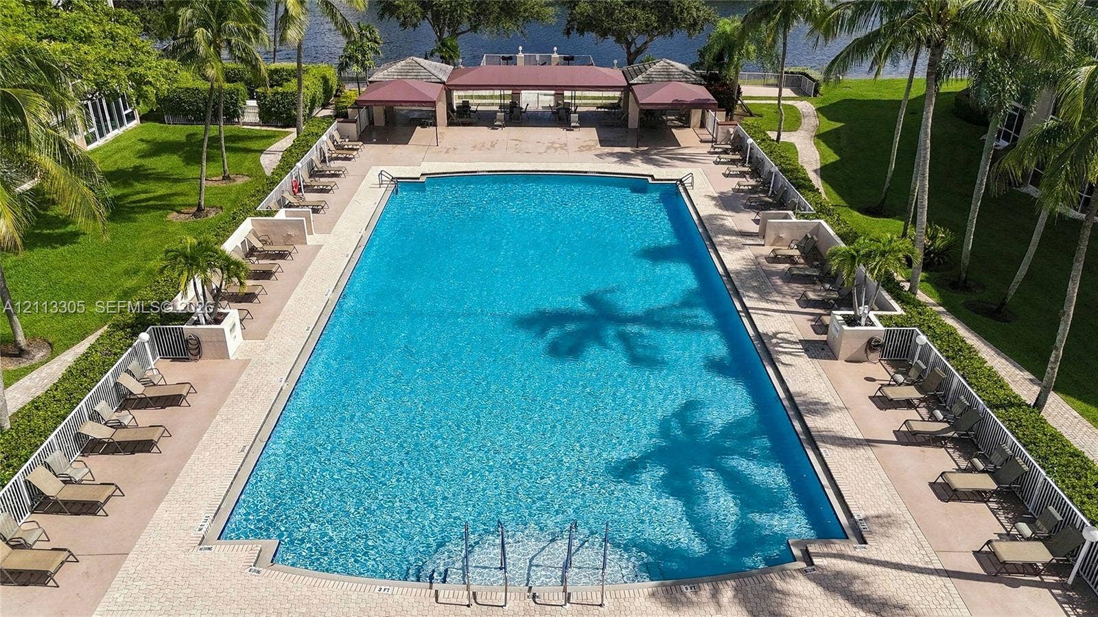 Rectangular swimming pool featuring a paved perimeter, masonry retaining walls, a covered pavilion with metal roofing, and mature palm landscaping