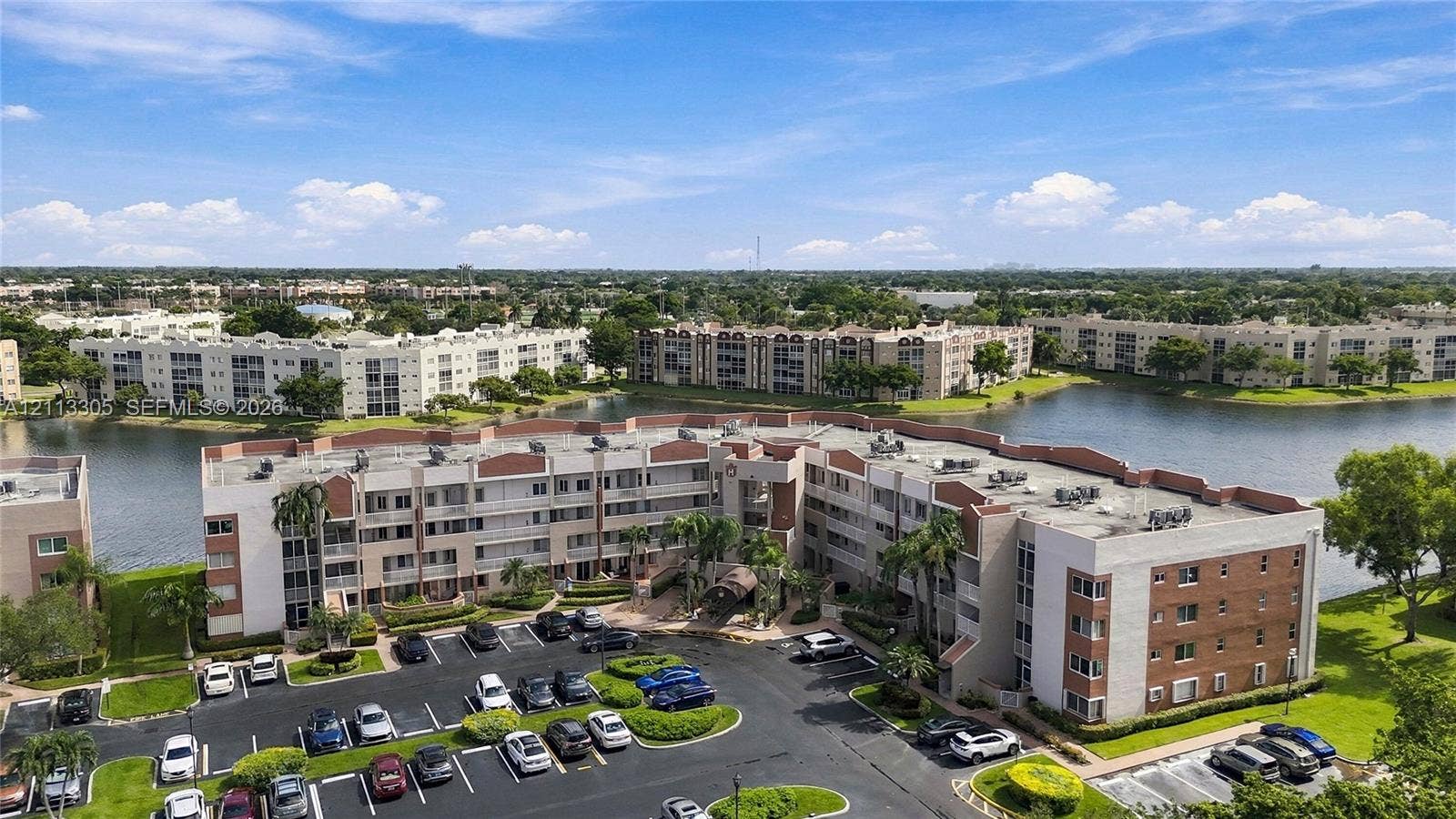 Aerial perspective of a multi-story residential building featuring masonry and stucco exterior, situated on a lakefront lot with surrounding water and landscaped green space