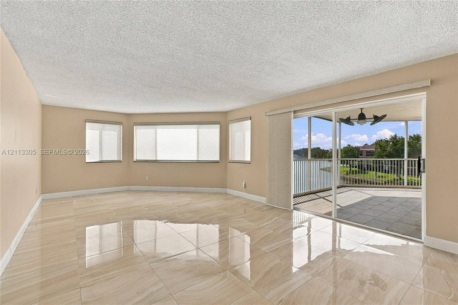 Living area featuring large-format tile flooring, expansive multi-pane windows, and a sliding glass door providing access to a screened-in balcony with ceiling fan