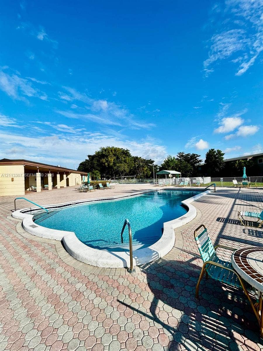 7605 NW 5th Place, #103, Margate, Margate, FL 33063 In-ground swimming pool featuring a curved concrete perimeter, metal handrails, and an expansive interlocking paver deck