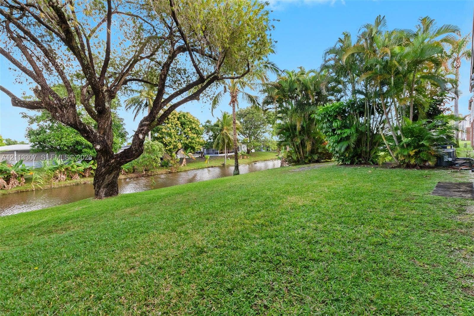 7605 NW 5th Place, #103, Margate, Margate, FL 33063 Waterfront lot featuring a grass lawn, mature trees, and established tropical vegetation