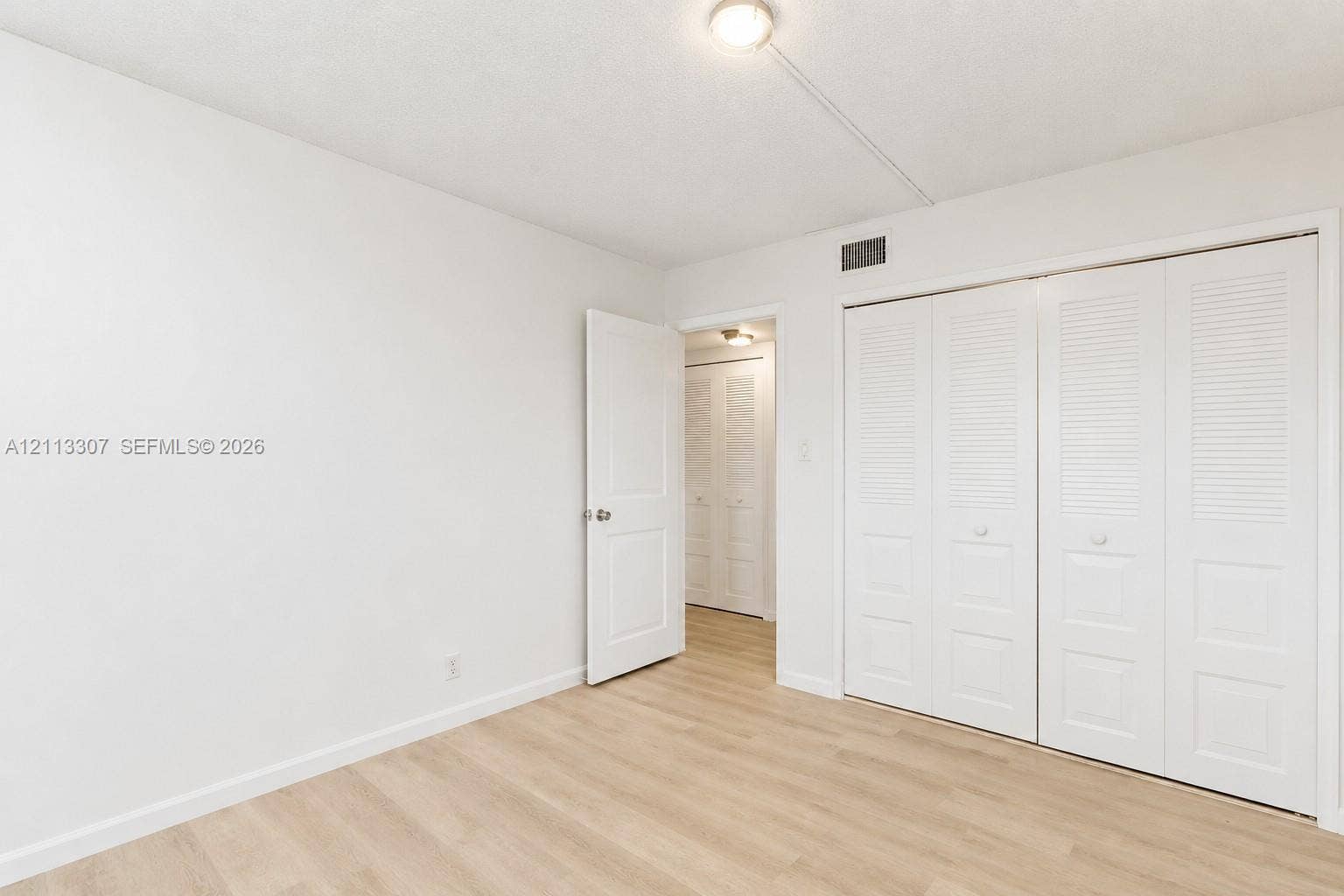 7605 NW 5th Place, #103, Margate, Margate, FL 33063 Neutral interior space featuring wood-finish flooring, white walls, flush-mount ceiling lighting, and built-in closet storage with louvered doors